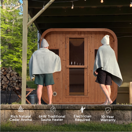 Two people in towels walking to the 4-Person Outdoor Traditional Cedar Sauna in a backyard