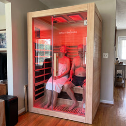 Couple sitting inside the 2-Person Red Light + Full Spectrum Hemlock Sauna in a living room