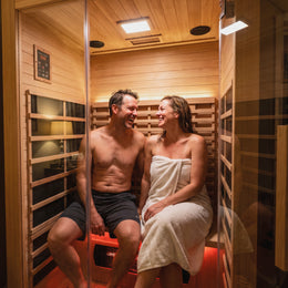 Couple smiling on the bench inside the 2-Person Red Light + Full Spectrum Hemlock Sauna