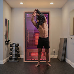 Man drying off next to the 1-Person Full Spectrum Hemlock Sauna in a home gym